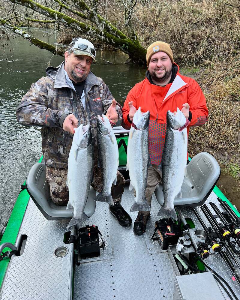 Two anglers each holding a pair of chrome steelhead on the boat
