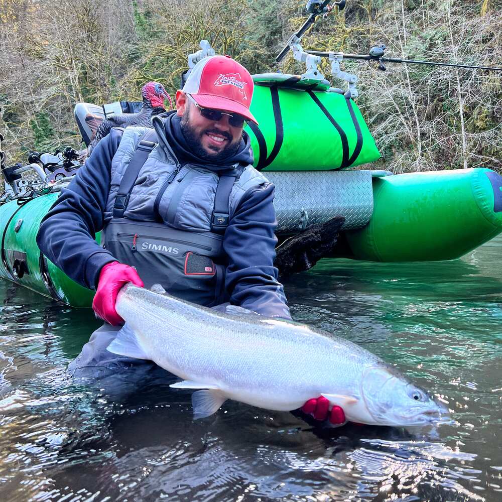 Angler in waders holding a bright steelhead on the boat